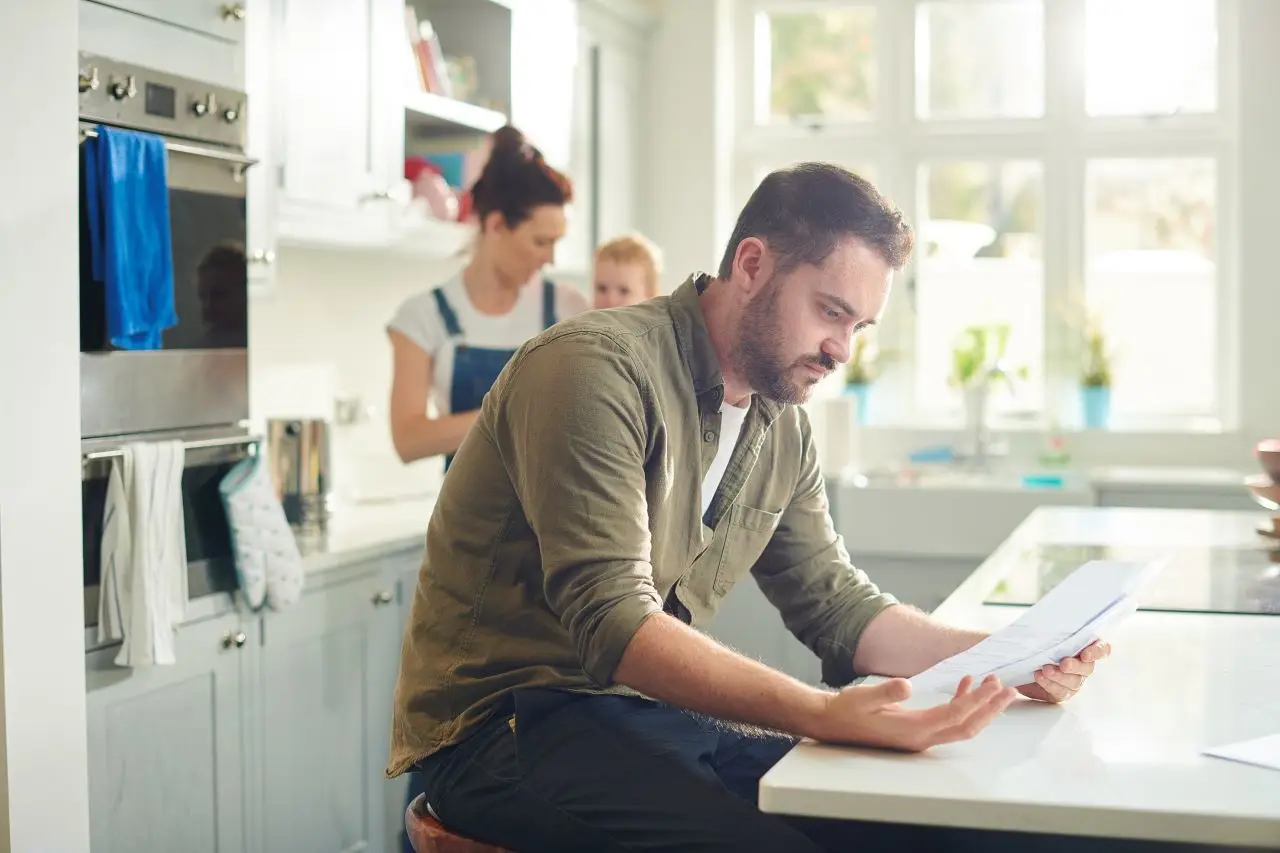 Young father looking over medical bills with his wife and young child in the background