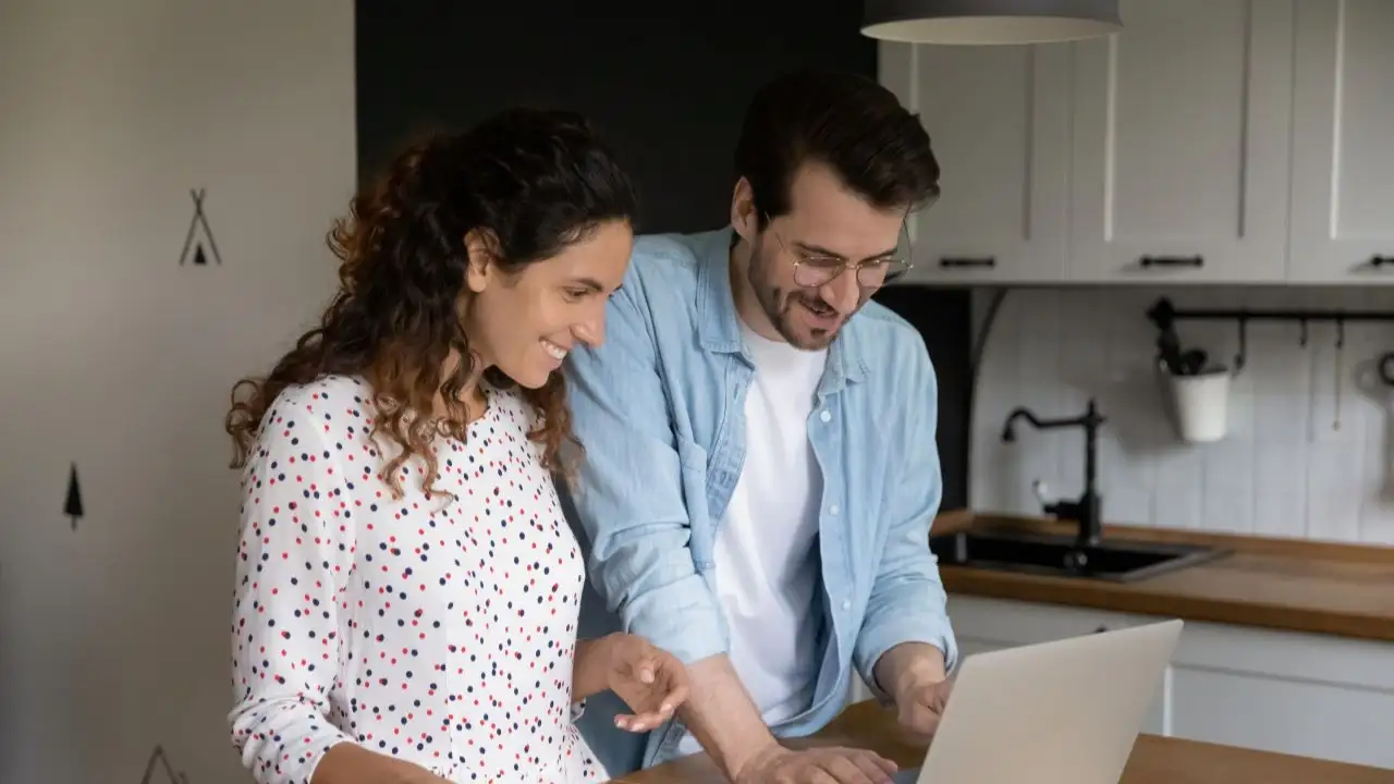 Happy bonding young married family couple using e-banking computer application, calculating domestic expenditures, planning future investment or vacation, paying utility bills online