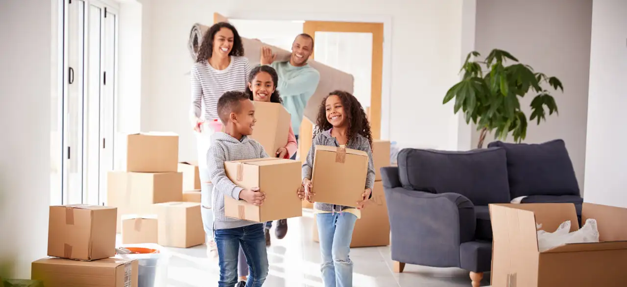 Smiling Family Carrying Boxes Into New Home On Moving Day