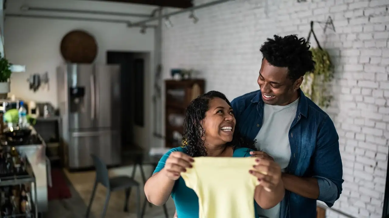 Pregnant couple holding a baby bodysuit at home