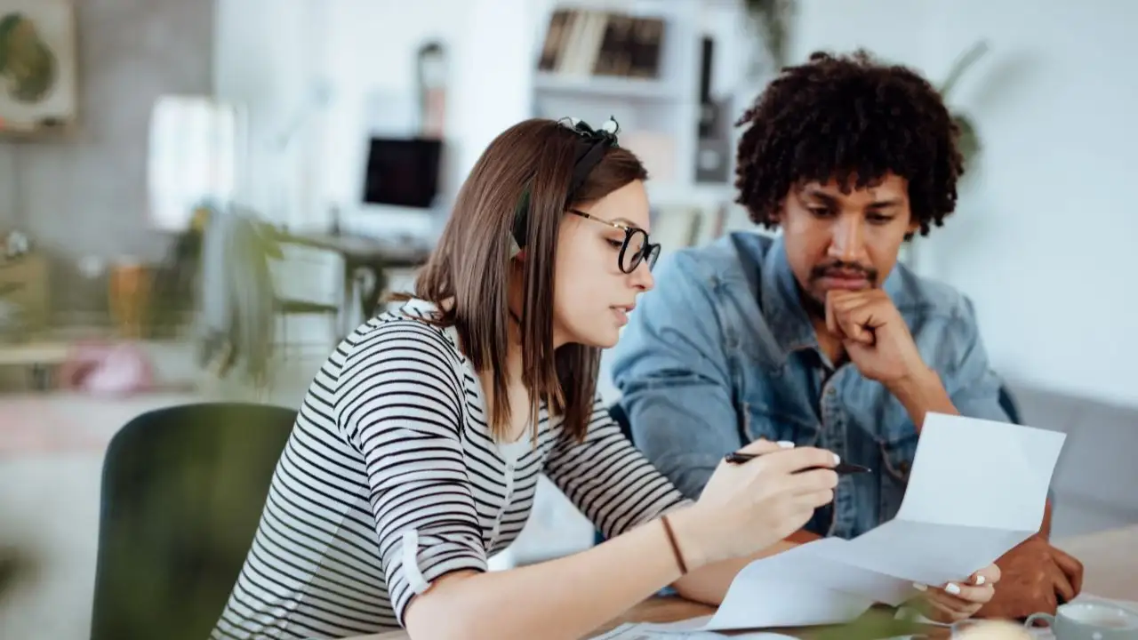 A young couple sitting a kitchen table looking at a budget and figuring out ways to pay off debt