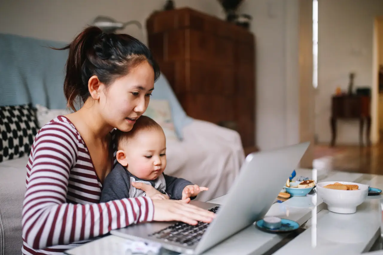 Portrait of a young Asian woman sitting at home, doing some freelance job while taking care of her little baby boy. 