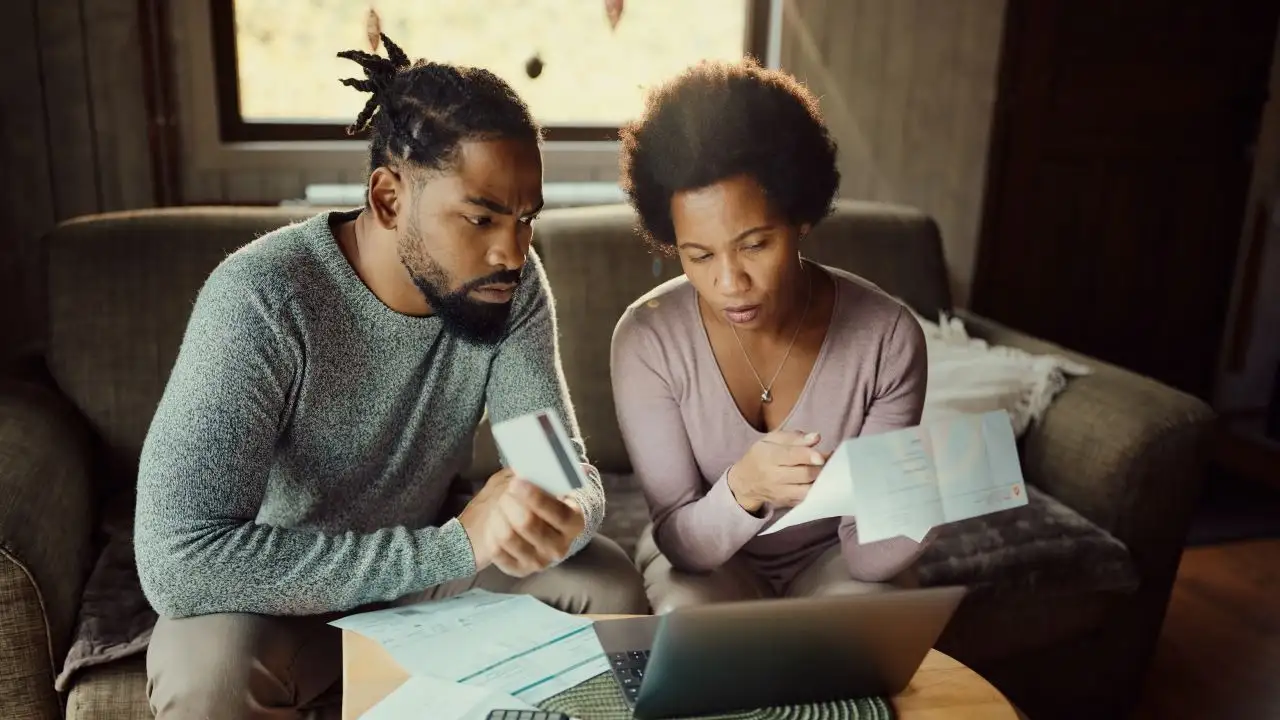 Worried African American couple using credit card while paying their bills online over laptop at home.