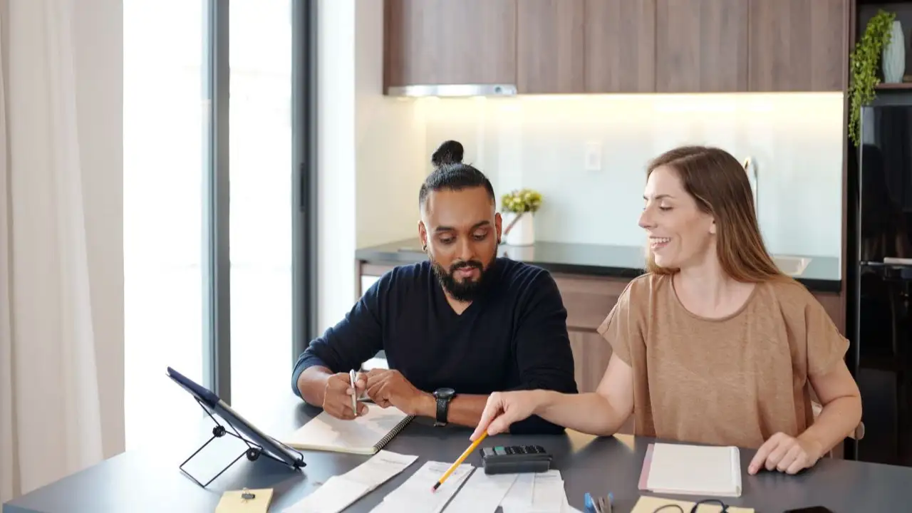 Smiling young woman pointing at bills on table and explaining to partner how to manage budget