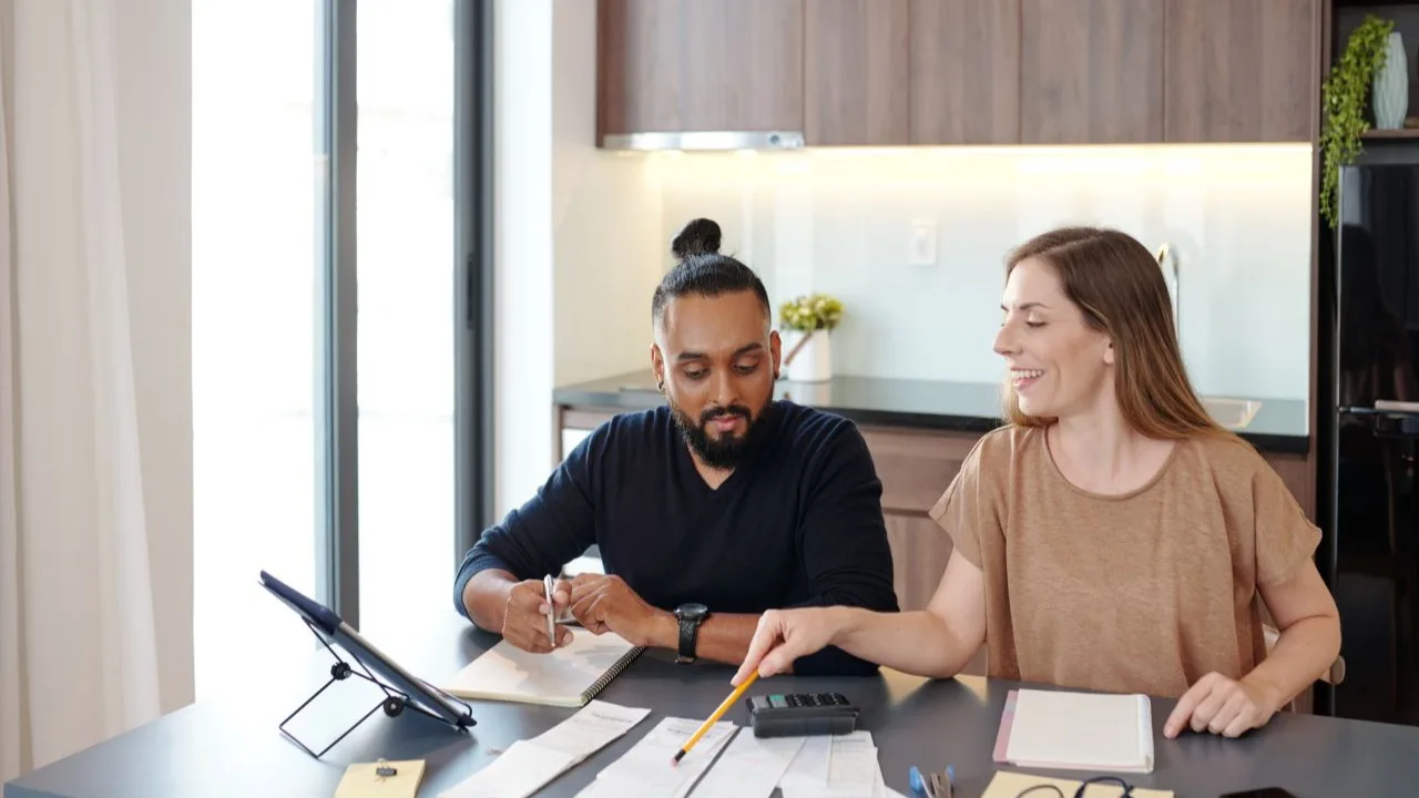 Smiling young woman pointing at bills on table and explaining to partner how to manage budget