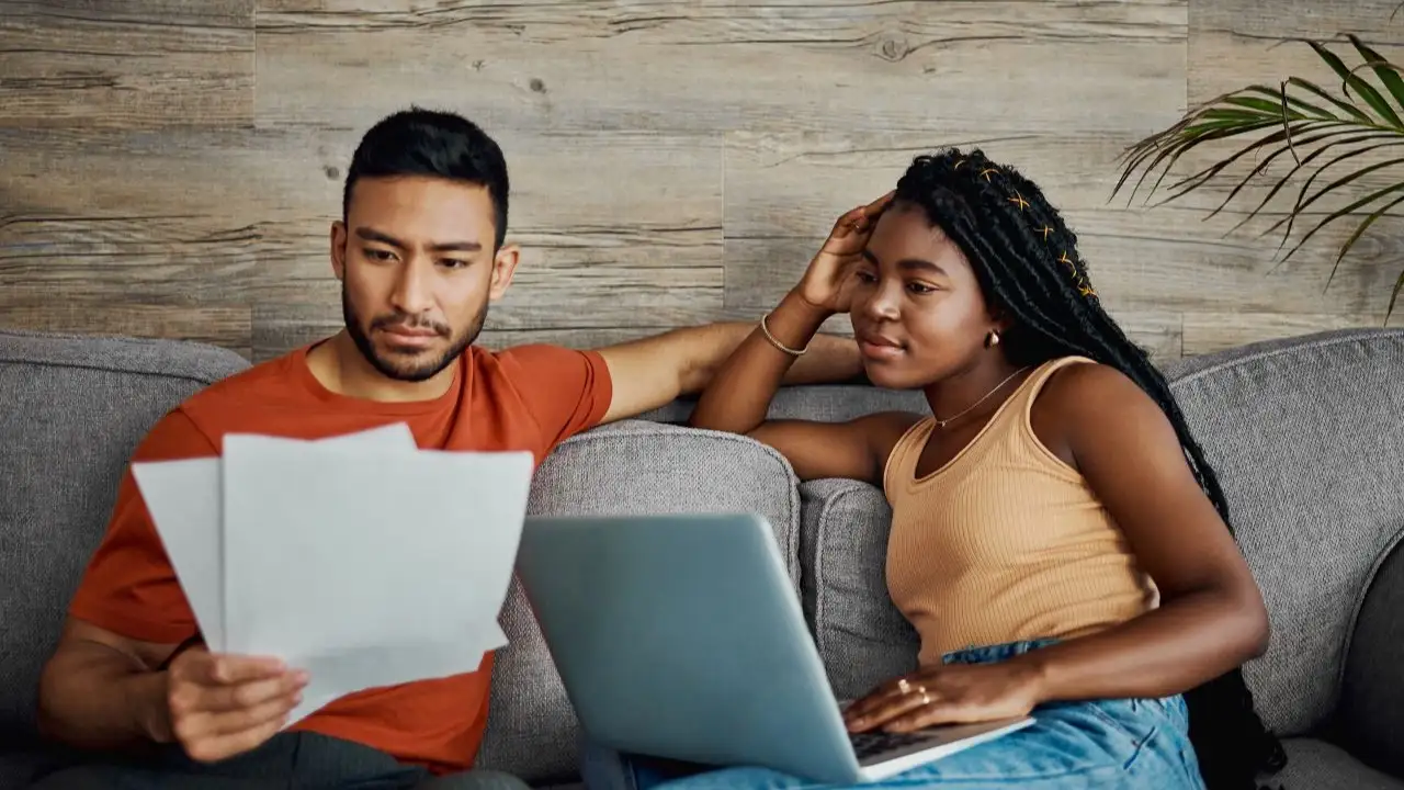 Shot of a young couple sitting in the living room at home and using a laptop to calculate their finances