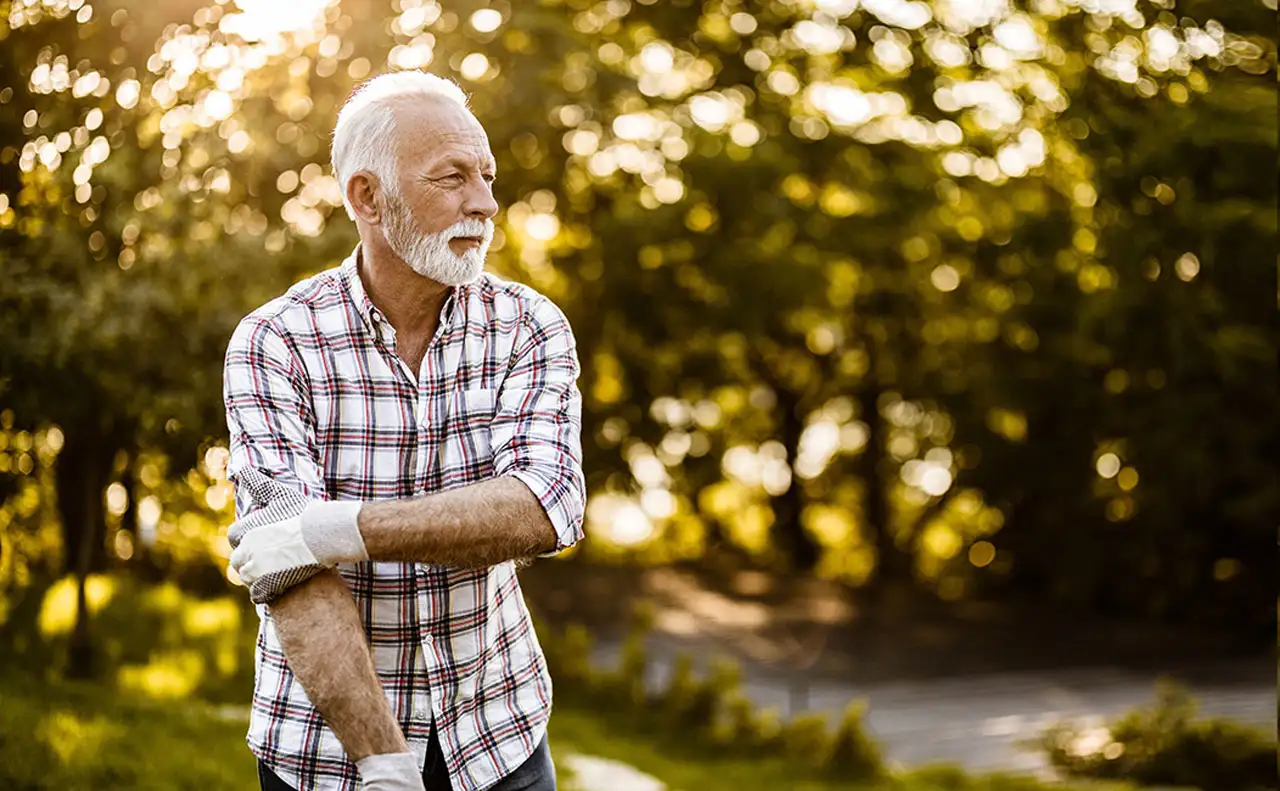 A man with a white beard and a plaid shirt doing gardening in his backyard