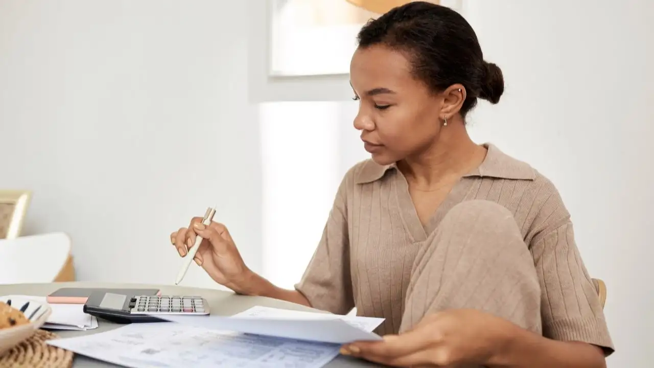 Young woman checking finances at home and using calculator 