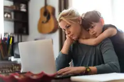 A cute little boy hugging his mom tightly while she is working.