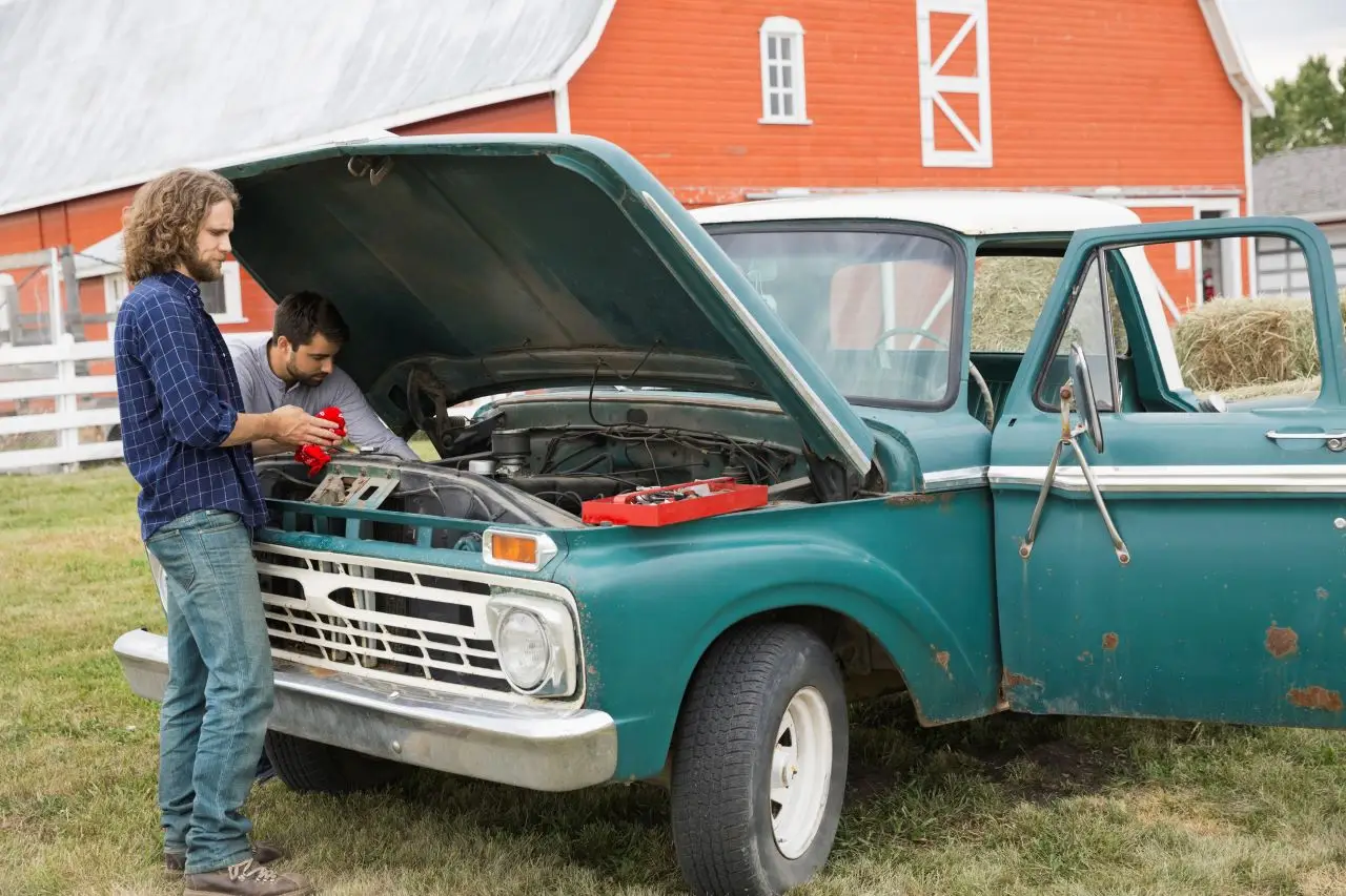 Men repairing pickup truck on farm 