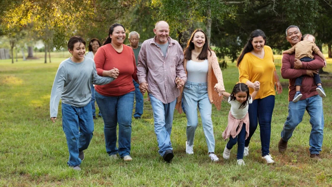 An extended family walking side by side holding hands, having fun together in a park or back yard, laughing.